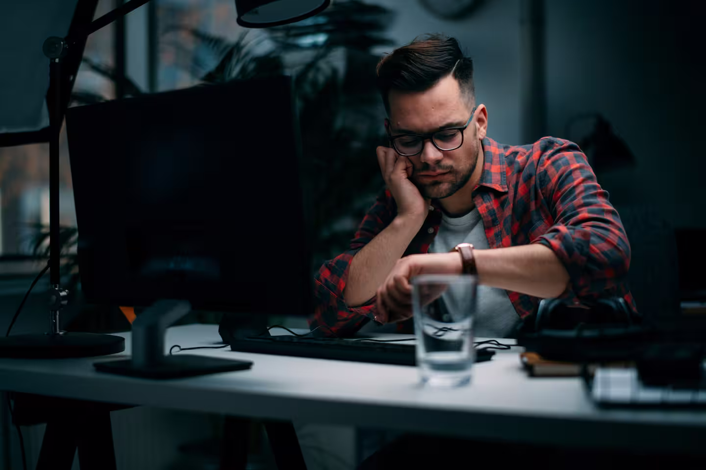 Guy at desk looking at watch looking frustrated